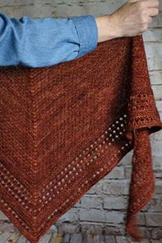 a person holding up a brown shawl in front of a brick wall