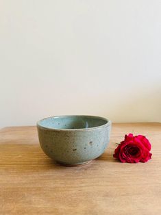 a small blue bowl with a red rose in front of it on a wooden table