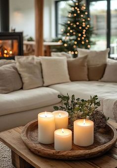 three lit candles sit on a wooden tray in front of a couch and christmas tree