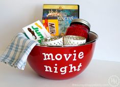 a red bowl filled with movies and other items on top of a white table next to a book