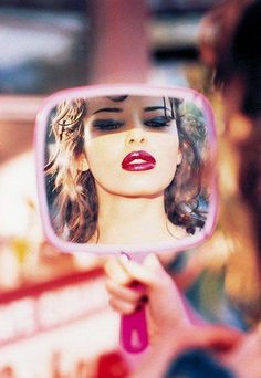 a woman is looking at her face in the mirror and she has red lipstick on