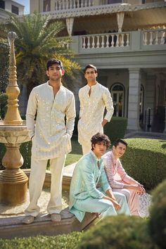 three men dressed in white standing next to each other near a fountain and building with balconies