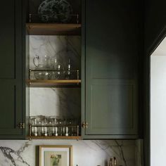 a kitchen with green cabinets and marble counter tops, an open shelf above the sink