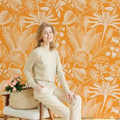 a woman sitting on a chair in front of an orange wall with flowers and leaves