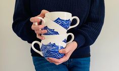 a person holding two coffee cups with waves painted on the mugs in their hands