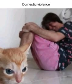 an orange and white cat laying on the floor next to a woman in pink shirt