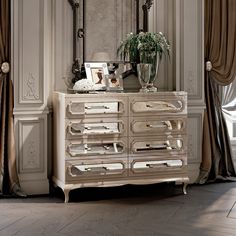 an antique dresser with mirror and vase on top in front of curtains, along with other furniture