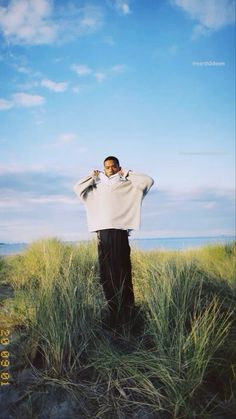 a man standing in tall grass with his hands on his head