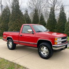 a red pick up truck parked on the side of a road in front of some trees