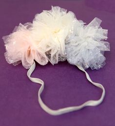 two white and light pink flower headbands on purple surface with ribbon around them