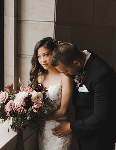 a bride and groom standing next to each other in front of a window holding their bouquet