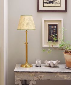 a table with a lamp, potted plant and pictures on the wall behind it