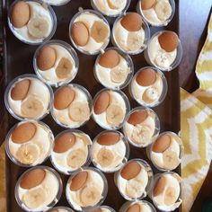 cupcakes with banana slices and cream frosting in plastic cups on a tray