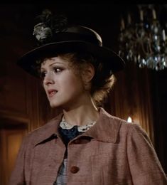 a woman wearing a hat and coat in a dark room with chandeliers hanging from the ceiling