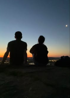 two people sitting on top of a hill watching the sunset