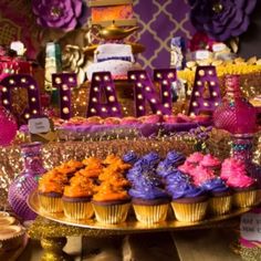 there are many cupcakes that are on the table with purple and gold decorations