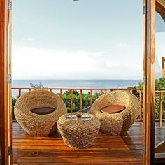 two wicker chairs sitting on top of a wooden deck next to an open door