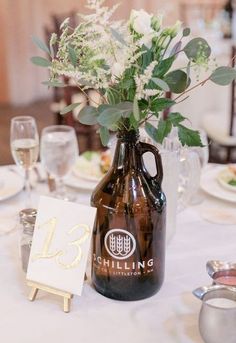 a brown jug with flowers in it sitting on top of a table next to plates and wine glasses