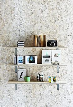 three shelves with books, pictures and photographs on them against a wallpapered background