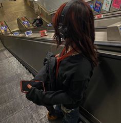 a woman with headphones on looking at her cell phone in an escalator