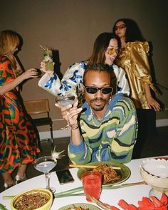 a group of people standing around a table with food and drinks in front of them