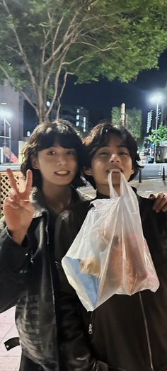 two young men standing next to each other holding up their peace signs and food bags