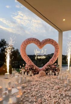 a heart - shaped flower arrangement is surrounded by candles and flowers at the end of an aisle