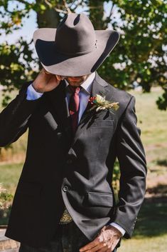 a man in a suit and cowboy hat is holding his hand to his face as he adjusts his hat