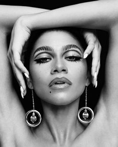 a black and white photo of a woman with her hands on her head, wearing large earrings