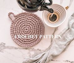 a crocheted pot holder next to a cup of coffee on a marble table