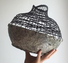 a hand holding up a wire covered vase