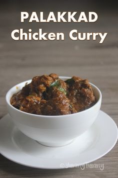 a white bowl filled with meat curry on top of a wooden table next to a plate