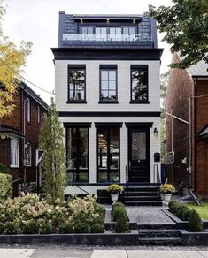 a white house with black windows and steps leading up to the front door is surrounded by landscaping