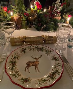 a white table topped with a plate covered in deer and pine cones next to candles