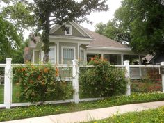 a white house with flowers growing on it's fence and bushes in the front yard