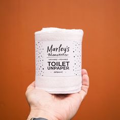 a hand holding a toilet paper roll in front of an orange wall with the words marfey's on it