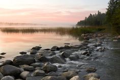 a river with rocks and water running through it at sunset or dawn, near some trees