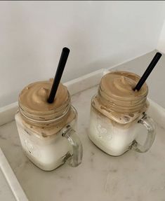 two mason jars filled with whipped cream and chocolate frosting, sitting on a marble tray