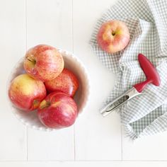 a bowl filled with red apples next to a pair of scissors on top of a table