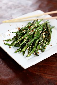 asparagus with sesame seeds and seasoning on a white plate next to chopsticks