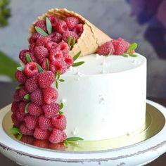 a white cake topped with raspberries on top of a wooden table next to an ice cream cone