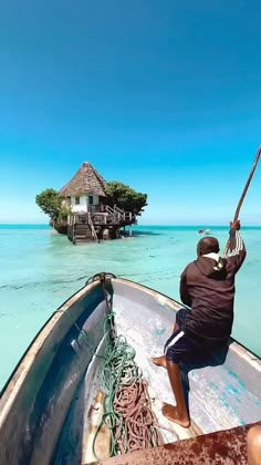 a man is sitting on the bow of a boat looking at an island in the ocean