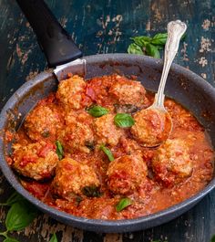 a skillet filled with meatballs covered in sauce and garnished with basil