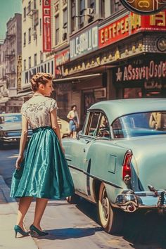 a woman standing on the sidewalk next to an old car