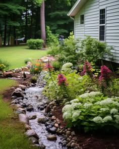 a small stream running through a lush green yard next to a white house with trees in the background