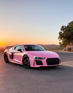 a pink sports car parked on the side of a road at sunset or sunrise with trees and hills in the background