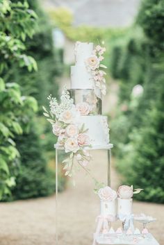 a three tiered wedding cake with pink flowers on the top and bottom is sitting on a table in front of some bushes