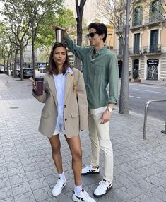 a man standing next to a woman holding a coffee cup in her hand on the street