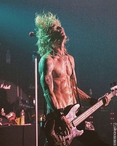 a shirtless man with long hair playing a bass guitar in front of microphones