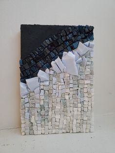 a piece of art made out of white and blue tiles on a wall next to a black square